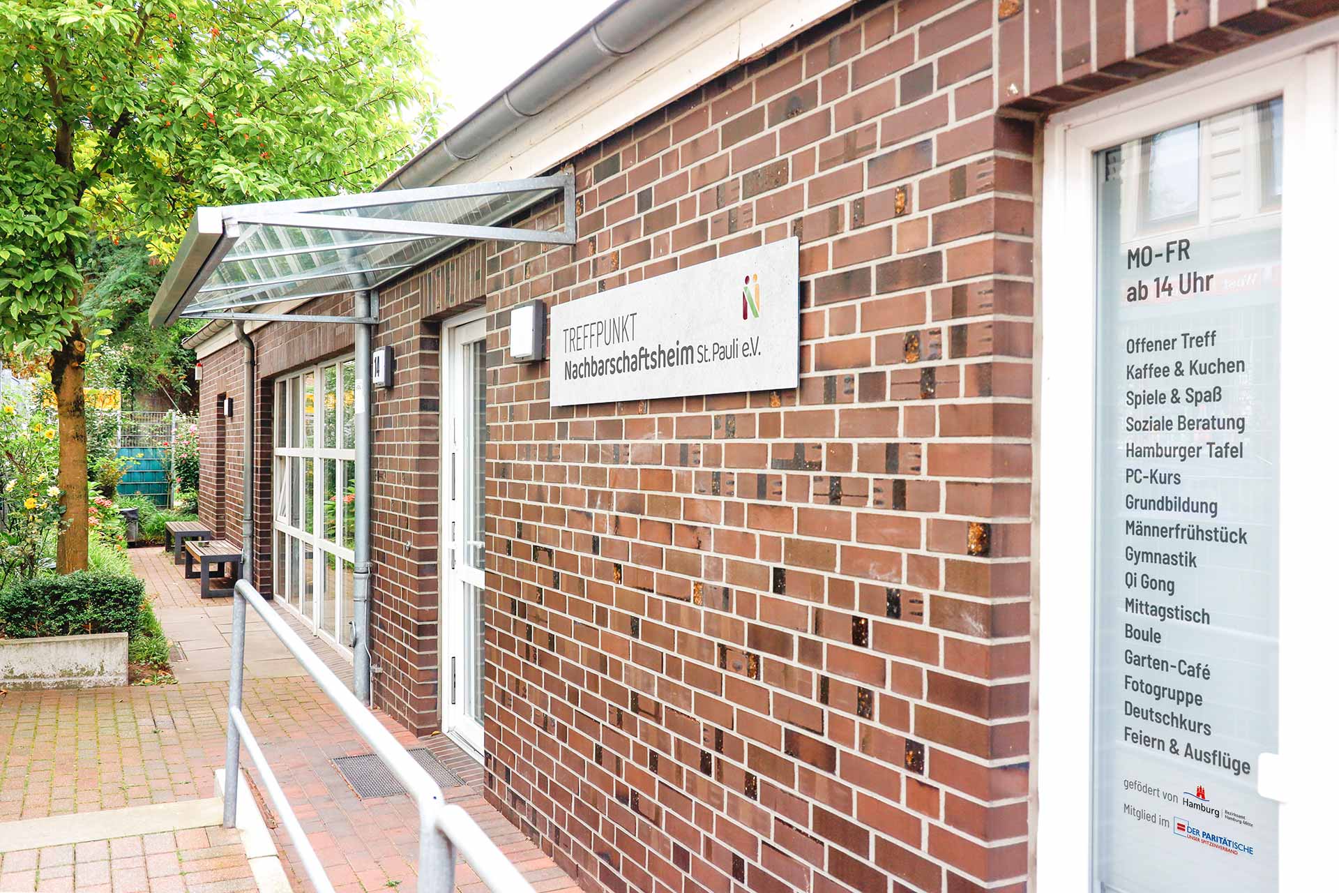 Außenansicht des Nachbarschaftsheims St. Pauli e.V. mit Eingang und Informationen zu den Angeboten wie Beratung, Freizeitaktivitäten und Kursen.
            